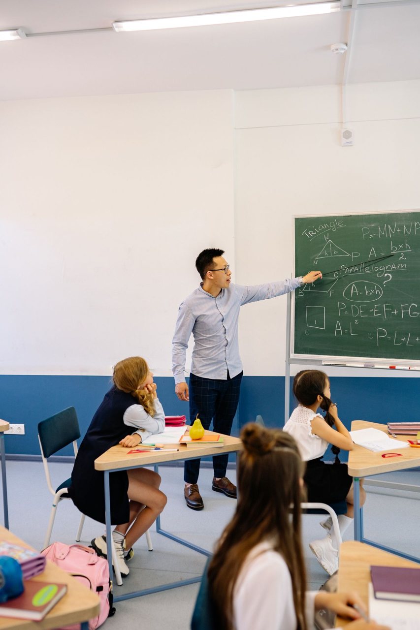 Free Teacher points to geometry equations on blackboard in a classroom setting. Stock Photo